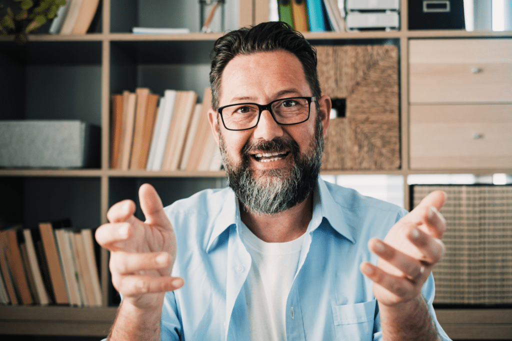 A bearded man with glasses making a gesture.