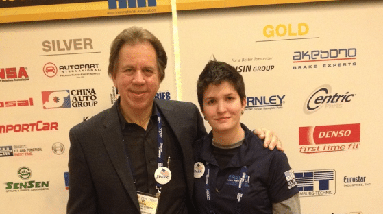 Two people standing together in front of a backdrop with various sponsor logos at a business growth event.