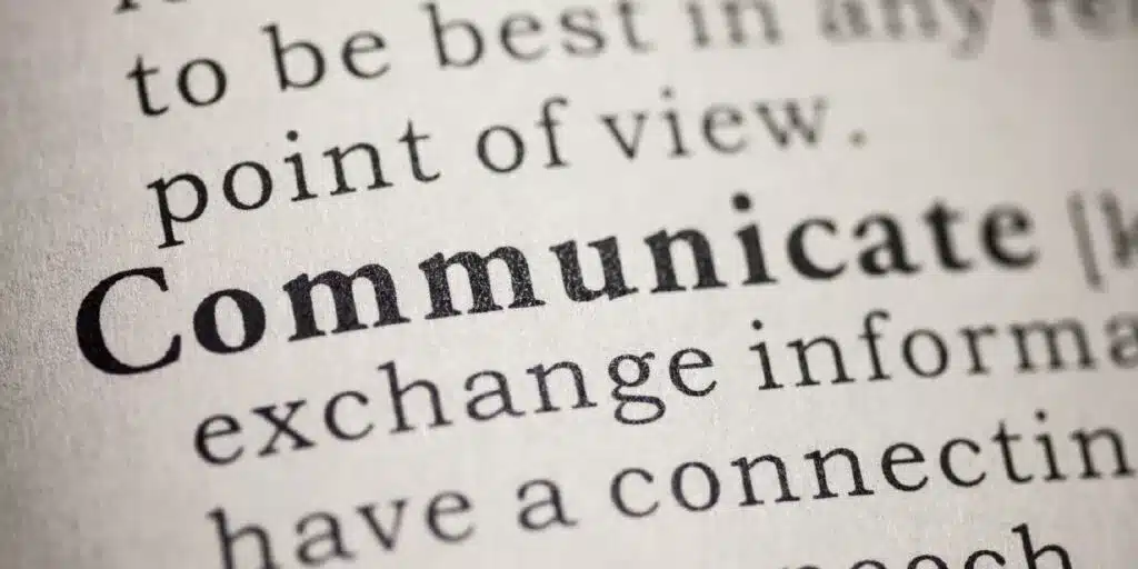 A close-up of a dictionary page highlighting the word "Communicate" in bold, with surrounding text slightly blurred, emphasizing the concept of exchanging information.