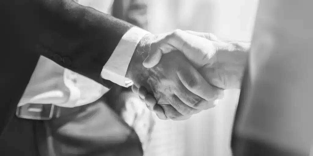A black and white close-up of two business professionals shaking hands, symbolizing agreement and partnership.