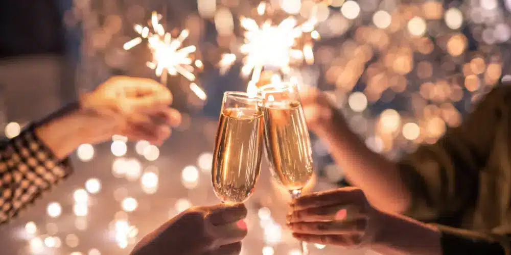 A festive image featuring people clinking champagne glasses while holding sparklers, surrounded by warm, glowing lights. The scene captures the essence of celebration, joy, and new beginnings.