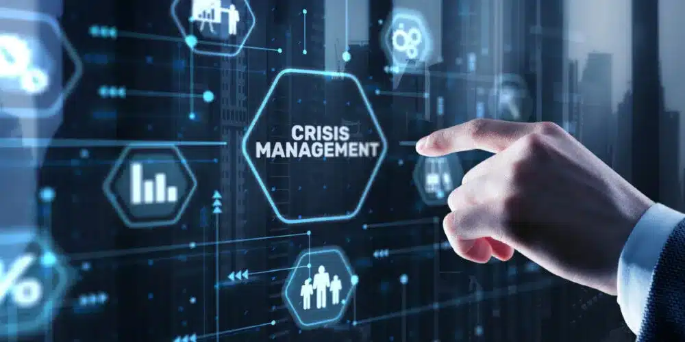 A businessman’s hand interacting with a futuristic digital interface displaying the words "Crisis Management," surrounded by technology-related icons, symbolizing strategic planning and response to business challenges.