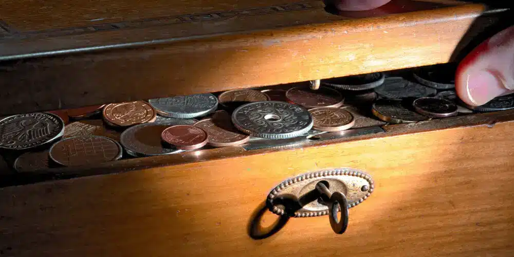 A close-up of an antique wooden treasure chest slightly open, revealing various old coins inside, with a hand peeking in, symbolizing hidden wealth or financial secrets.